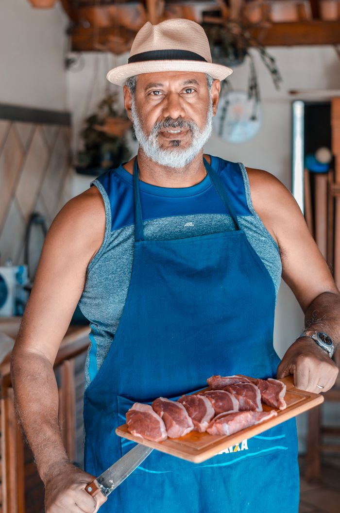 Middle-aged man holding sliced meat on a wooden board in a cozy kitchen.