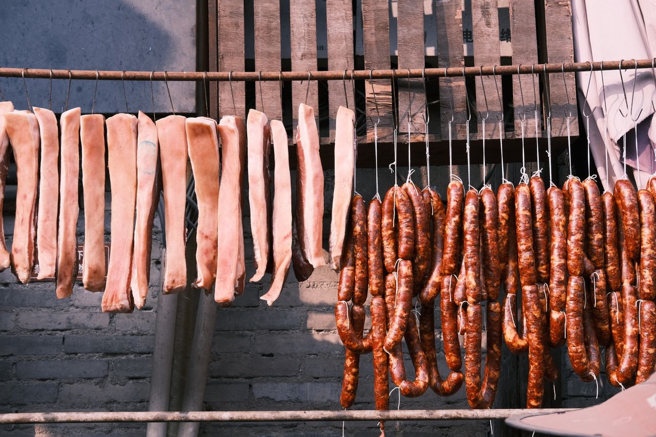 Raw meat strips and sausages drying outdoors, showcasing traditional food preservation methods.