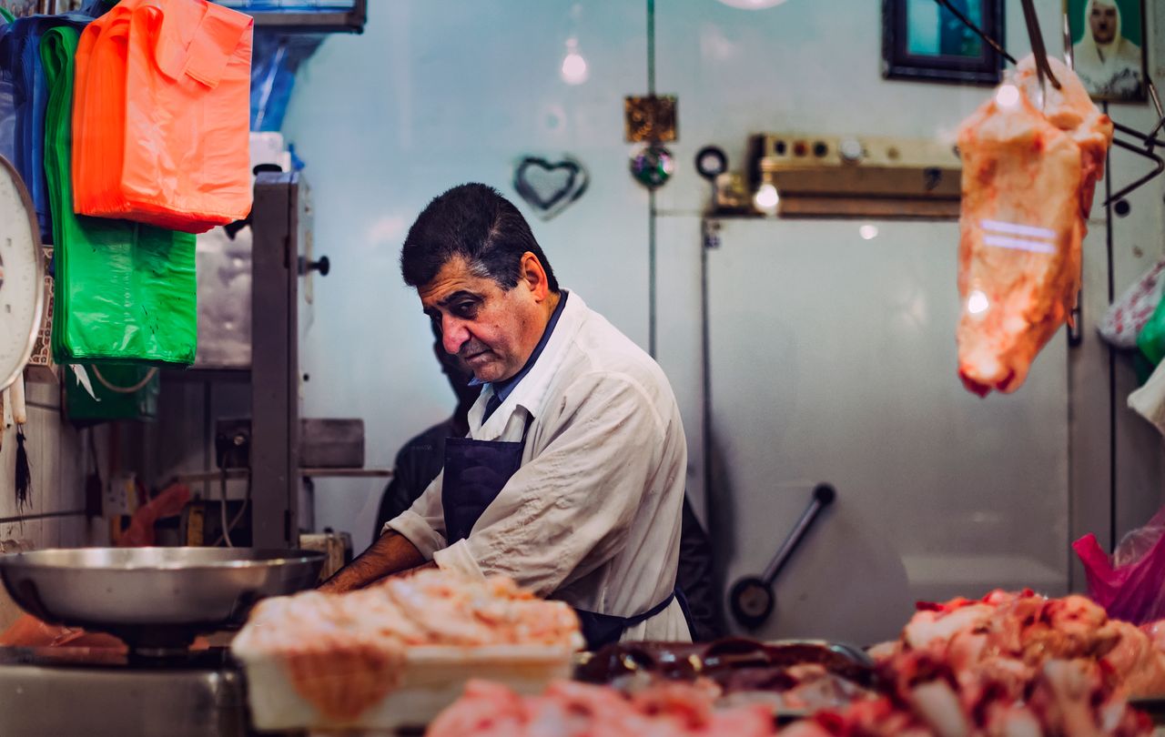 A butcher cuts meat at a market stall in Doha, Qatar, showcasing traditional butchery skills.